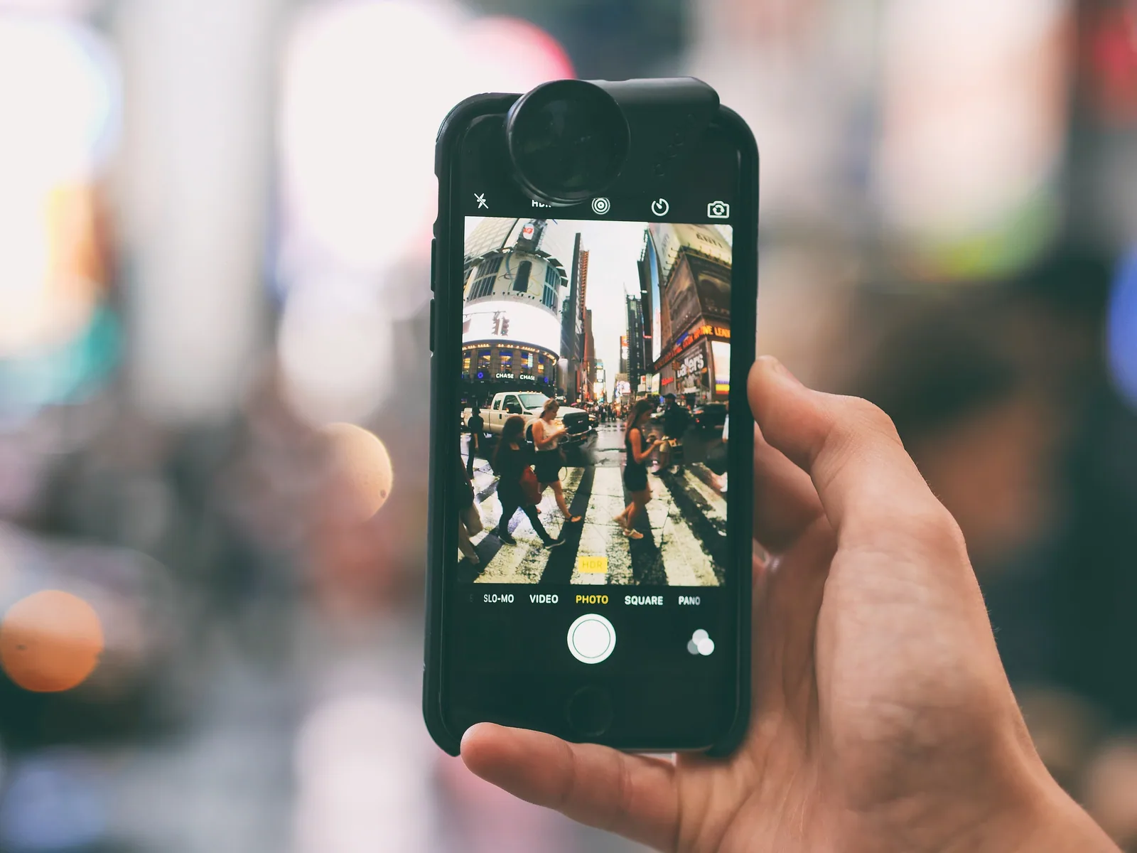 A hand holding up a phone to photograph a busy Theater District street in Manhattan